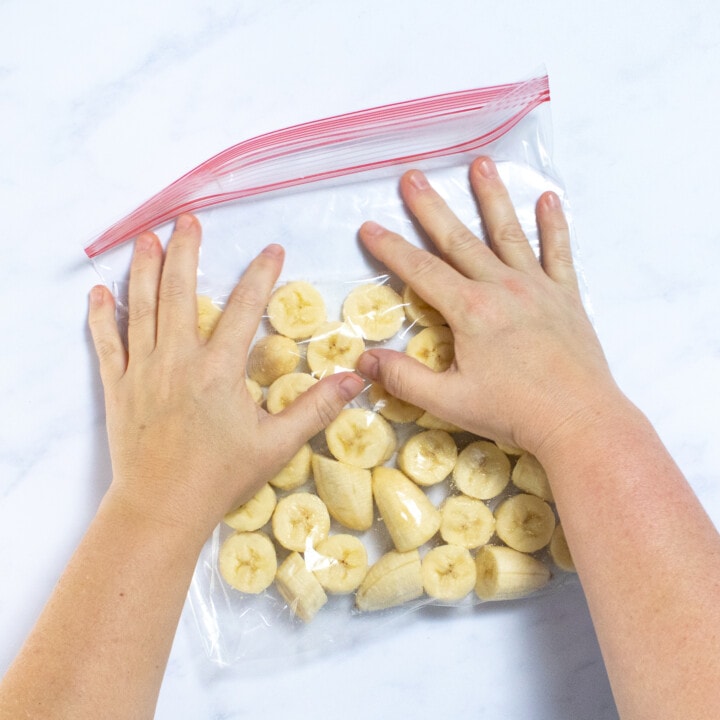 Two hands deadly percent of Erica Ziploc bag full of sliced bananas.