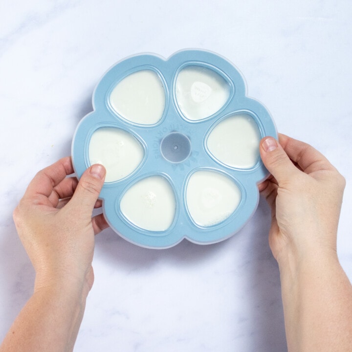 Two hands putting a lid on a freezer tray of milk.