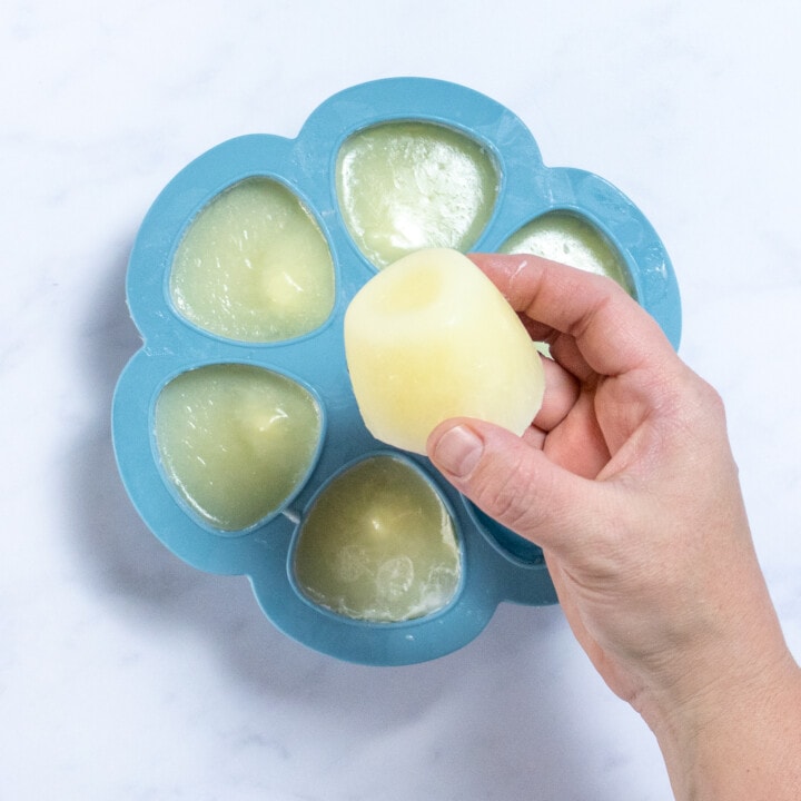 A hand holding a frozen milk cube against a tray of frozen milk.