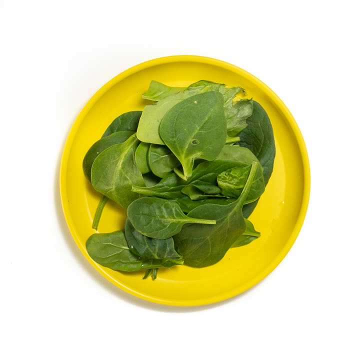 Yellow plate with spinach leaves on top. 