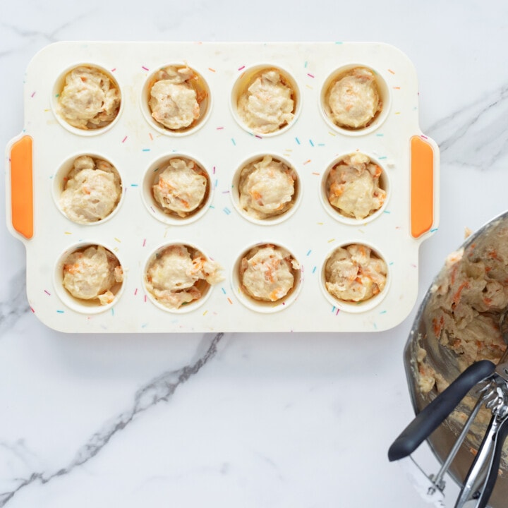 A colorful muffin pan been filled with the batter of muffins for baby and toddler against a marble backdrop.