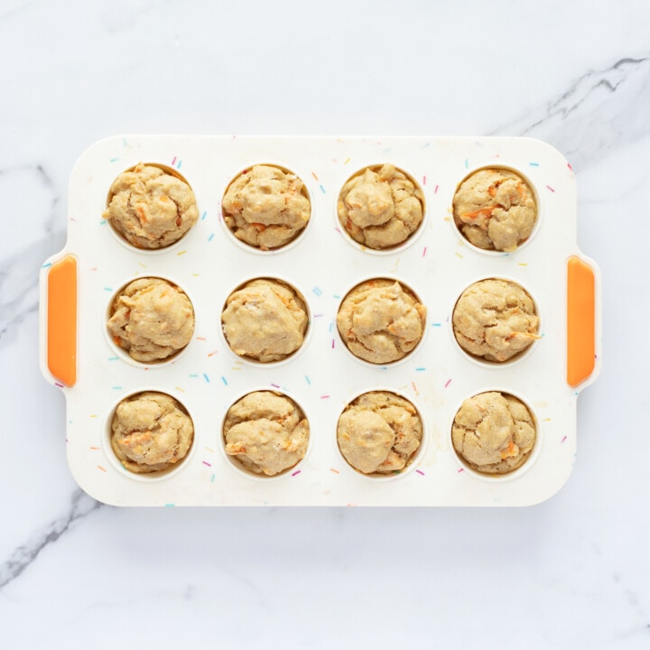 A colorful muffin tray with ABC muffins made with apple, banana and carrots I can see marble countertop.