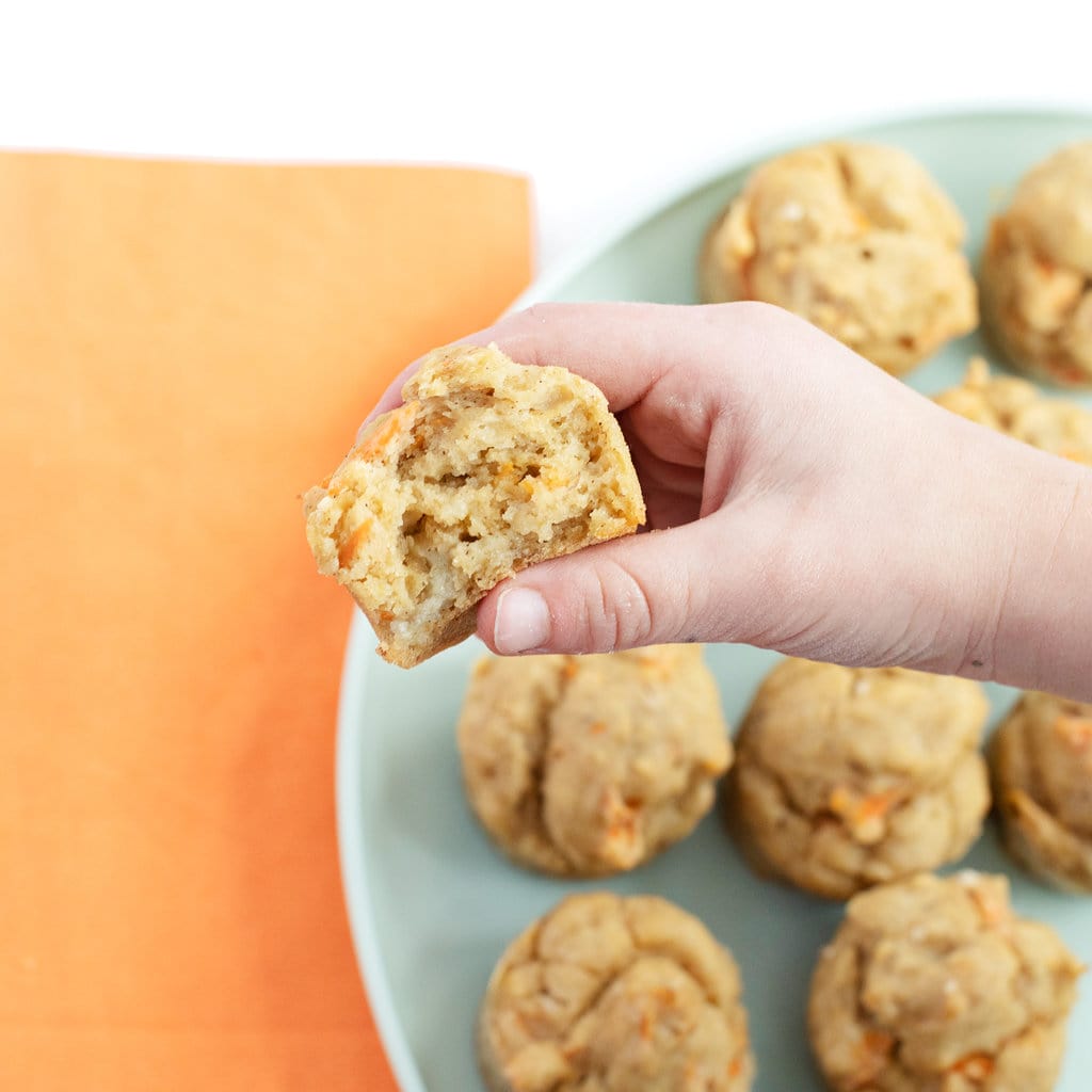 Small toddler hand holding an ABC muffin over a plate of muffins with a colorful napkin.