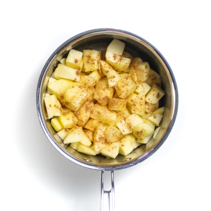 Silver sauce pan on a white background with raw chopped apples and sprinkled with cinnamon.