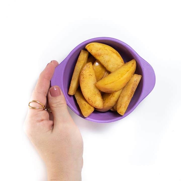 Hand holding a purple bowl with sautéed apples slices.