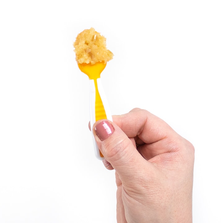 Hand holding up a self serving spoon with apples for baby.