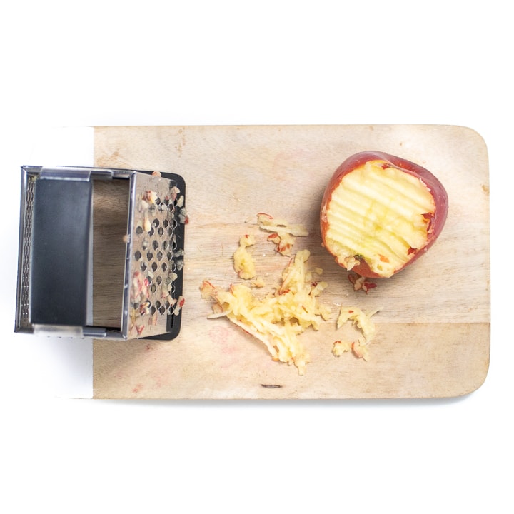 cutting board with an apple being grated.