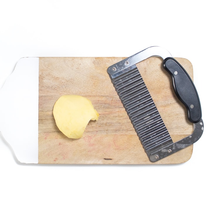 cutting board with an apple and a waffle knife.