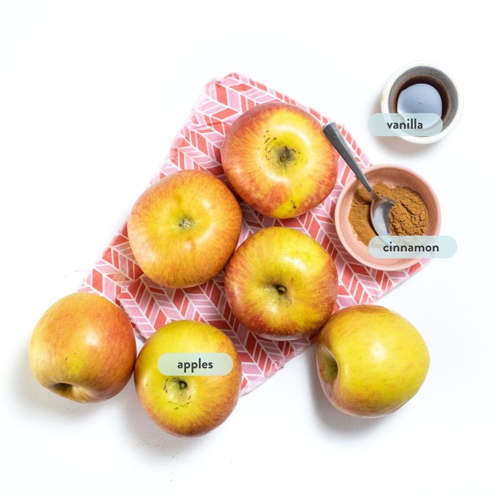 Spread of ingredients on a pink napkin on a white counter for homemade applesauce with graphics next to each one.