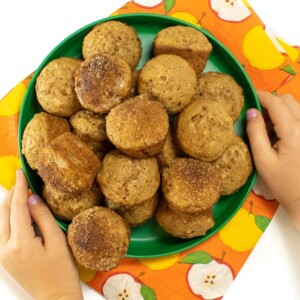 small kids hands holding a green plate of mini muffins.