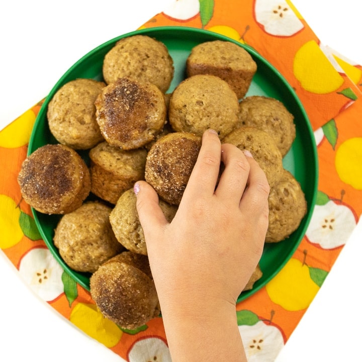 Green plate with small toddler hand reaching for a mini muffin.