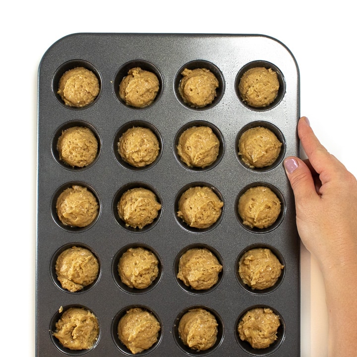 Hand holding mini muffin tin full of applesauce muffins.