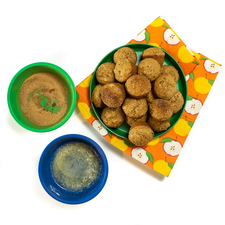 Plate of mini applesauce muffins getting a sprinkle of cinnamon and sugar.