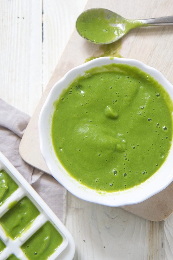 white bowl of asparagus puree, sitting on a wooden cutting board on top of a white wooden board