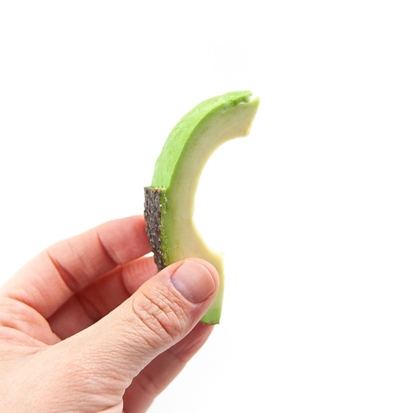 Hand holding a wedge of avocado.