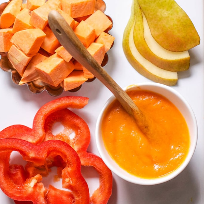 A spread of produce surrounding a small white bowl filled with baby food puree. 