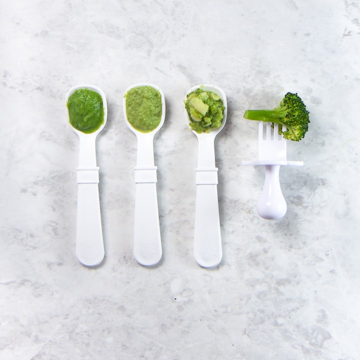 Lineup of spoon and a fork with different stages of baby food on it.