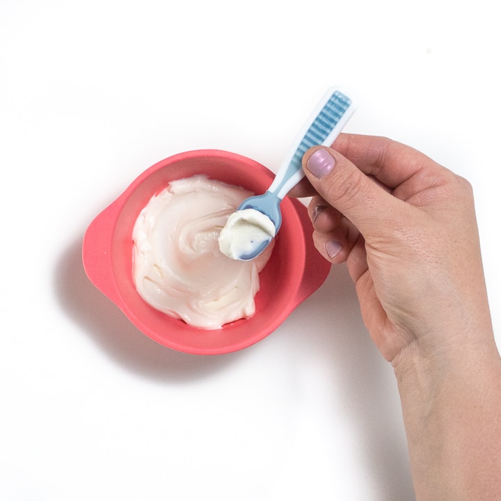 Hand holding a baby spoon with yogurt on it.