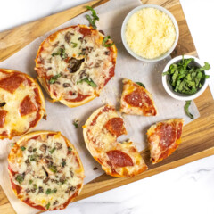 Cutting board with bagel pizzas Parmesan and basil cut into wedges.