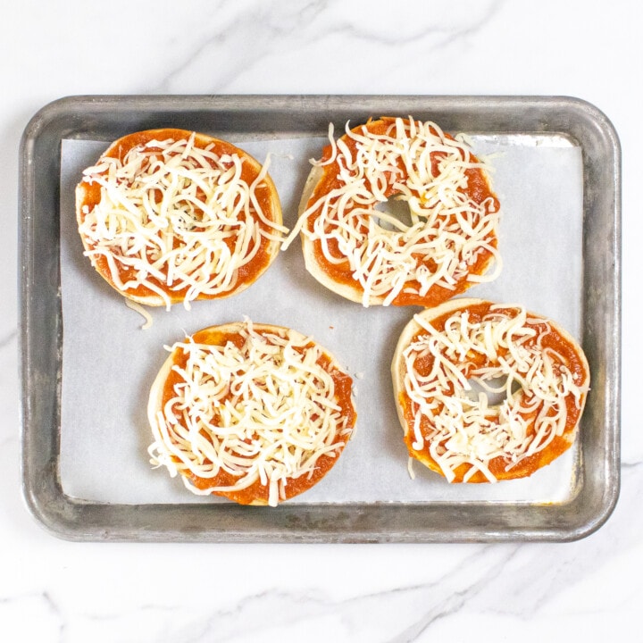 Pizza bagels with cheese and tomato sauce getting ready to go into the oven and bake.