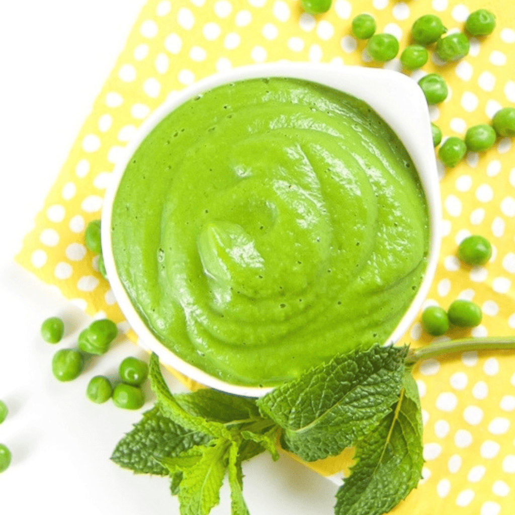 White bowl filled with a smooth pea puree. The bowl is on a yellow napkin on my white kitchen counter with a scattering of peas and mint.