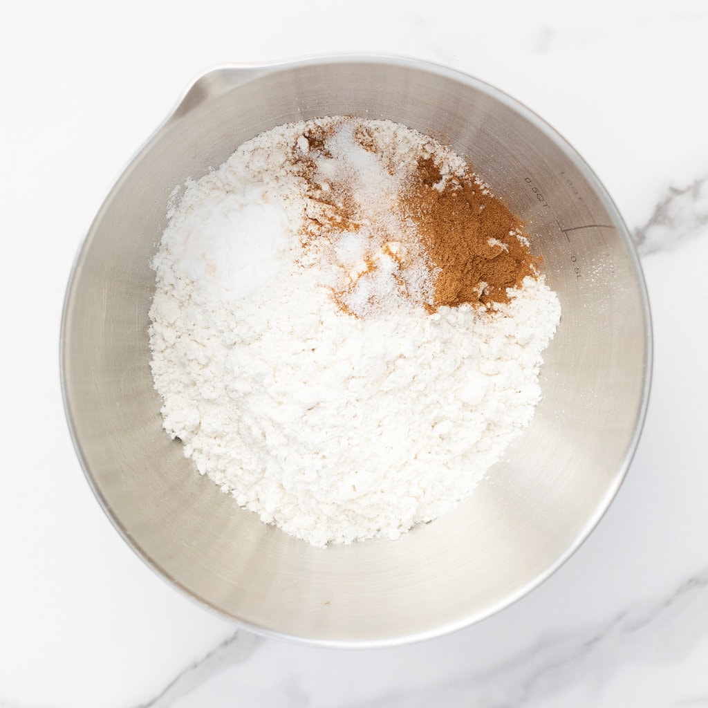 Silver mixing bowl with flour and baking ingredients against marble countertop.