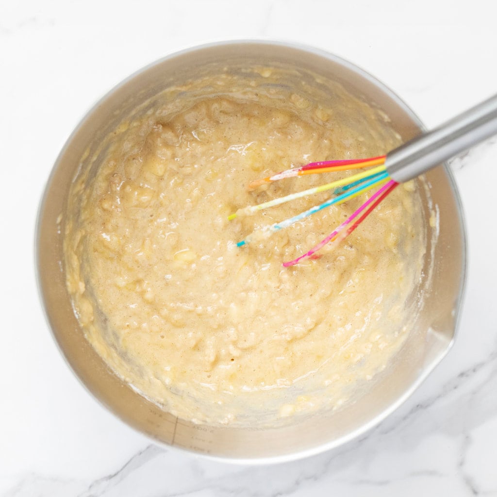 Silver mixing bowl, with muffin batter inside against a marble countertop.