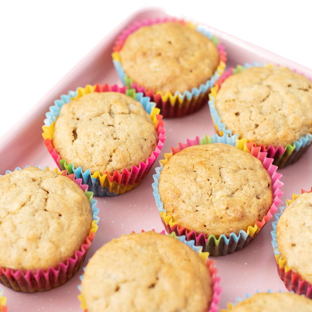 Pink tray with banana muffins lined up in colorful muffin wrappers.