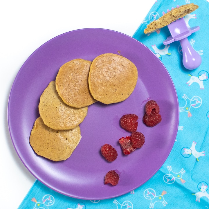 Purple plate with banana pancakes and raspberry pieces for baby.