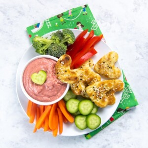 bowl of beet hummus with plate full of chopped veggies and cut-out heart pita bread.