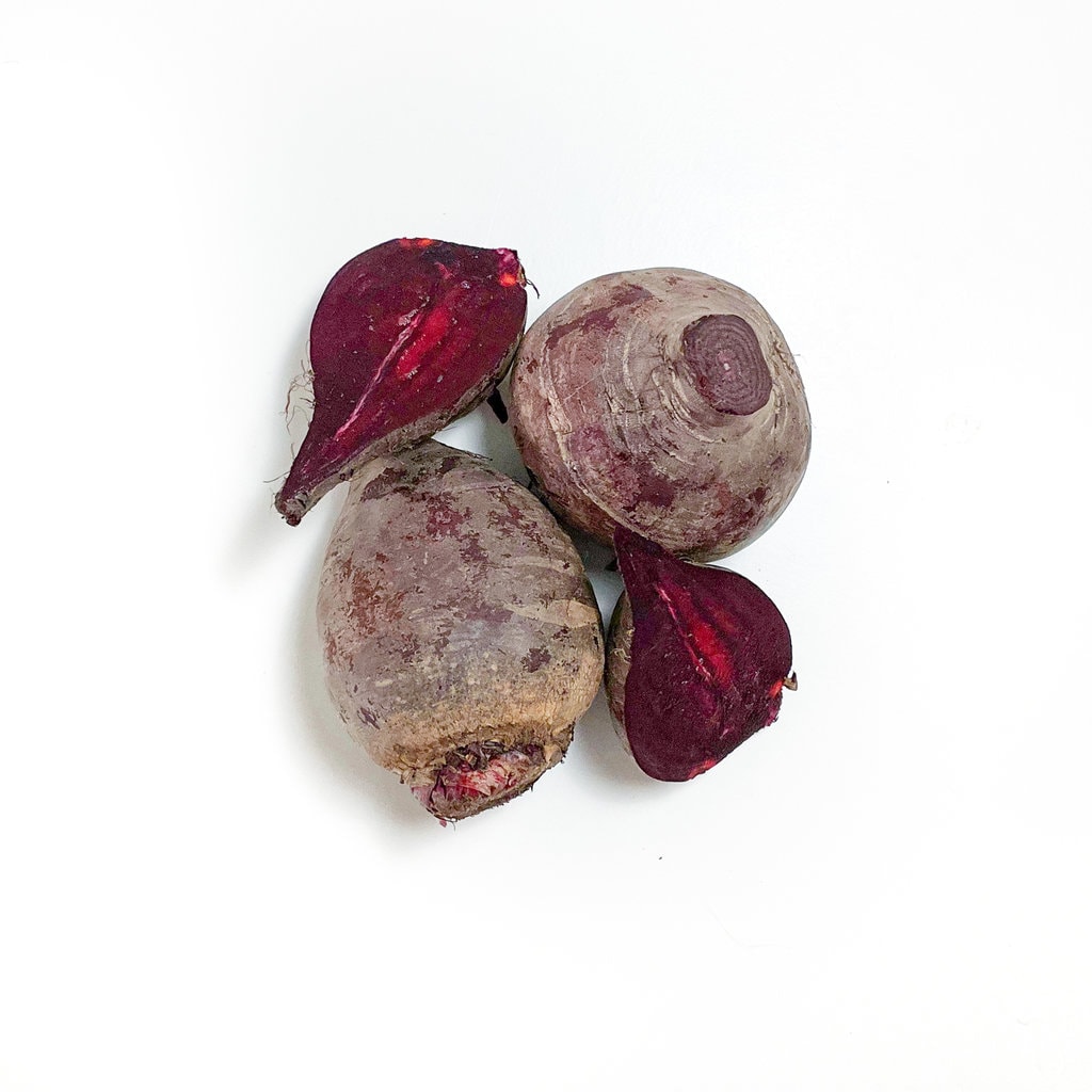 Pile of beets on a white counter, some of them whole and some of them cut.