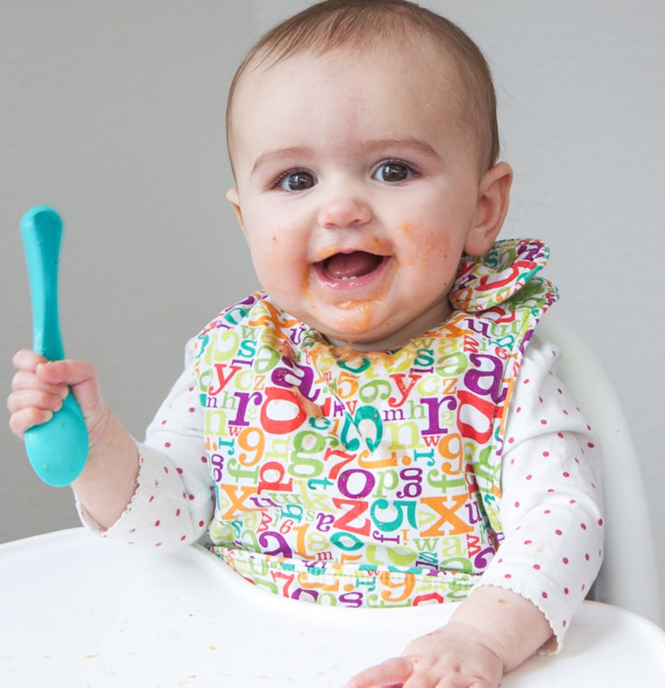 Baby in highchair with baby puree all over her face.