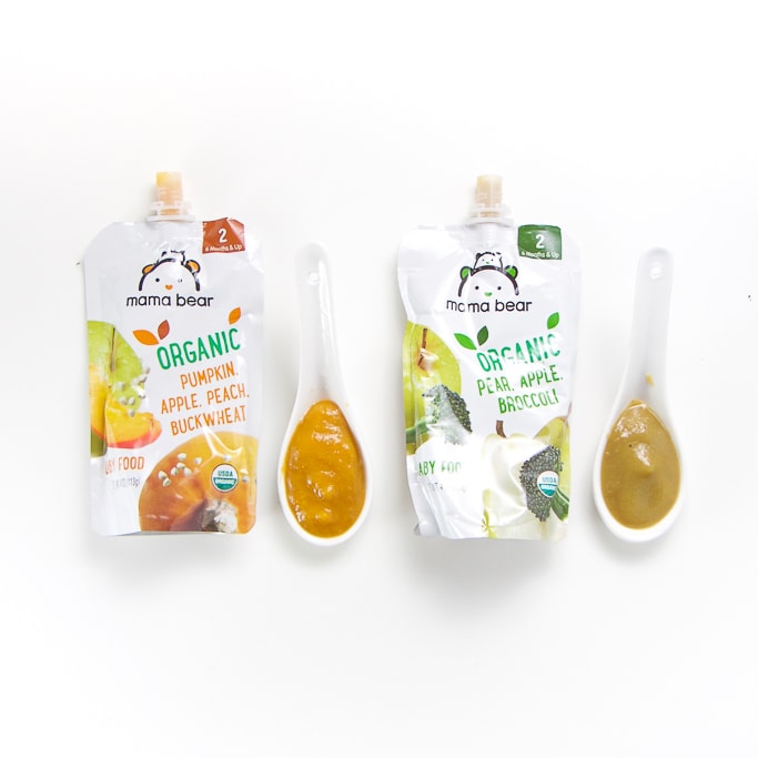 2 Mama Bear baby food pouches with spoons next the them with puree inside.