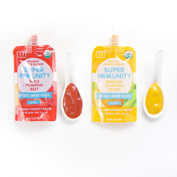 2 organic NuturMe baby food pouches with spoons next the them with puree inside.