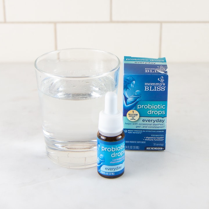 A box and a bottle of Mommy's Bliss probiotics in front of a glass of water.