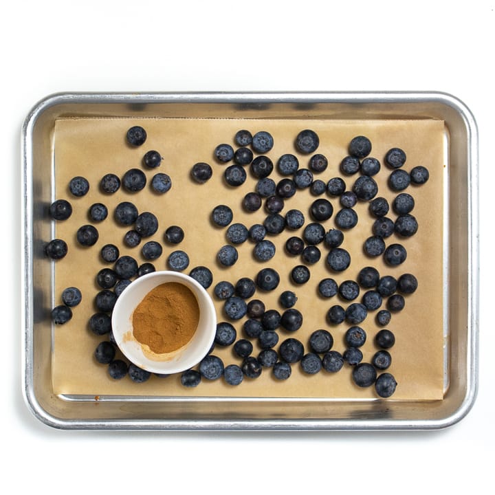 A baking sheet with blueberries and a small bowl of cinnamon.