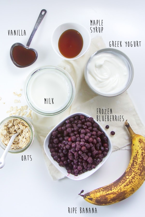 Oats, banana, blueberries, milk, yogurt, vanilla, and maple syrup flat lay