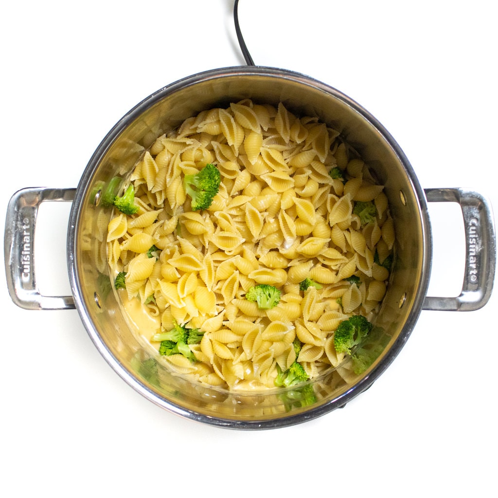 A large silver pot with broccoli mac & cheese about to get mixed in with the cheese sauce.