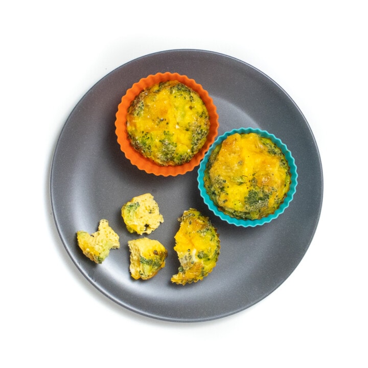 Gray baby plate filled with 2 full broccoli cheese cups and one broken into smaller pieces.