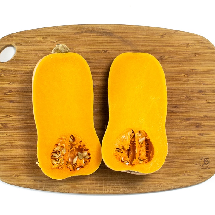 A butternut squash cut in half sitting on a cutting board. 