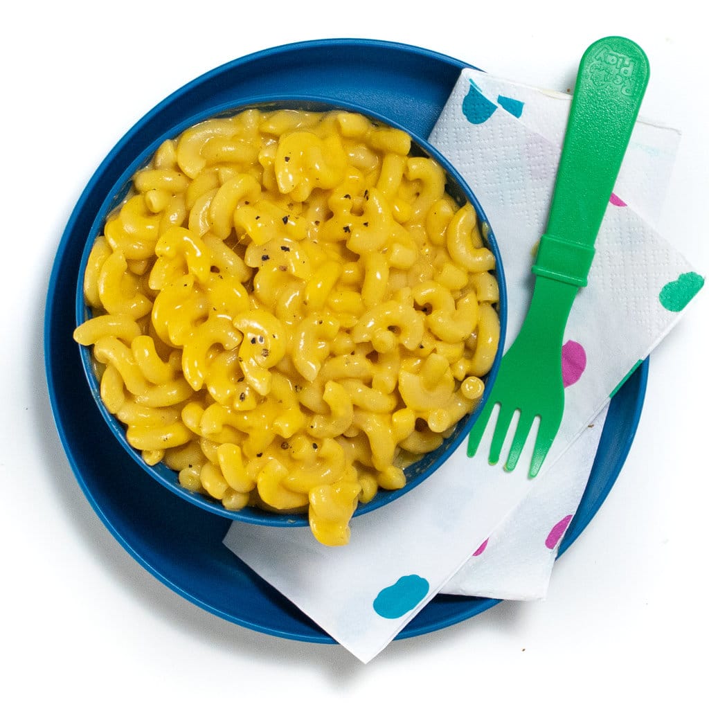 A blue kids plate and bowl filled with butternut squash mac & cheese with a colorful napkin and a green fork.