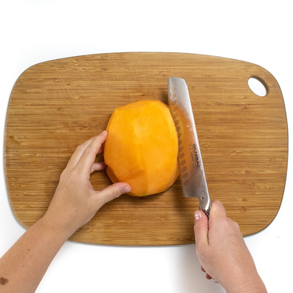 Hands holding a Cantelope in a knife cutting it into thick wedges.