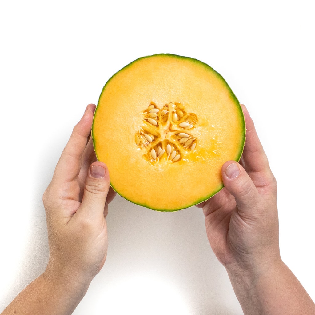 Two hands holding a cantaloupe cut in half