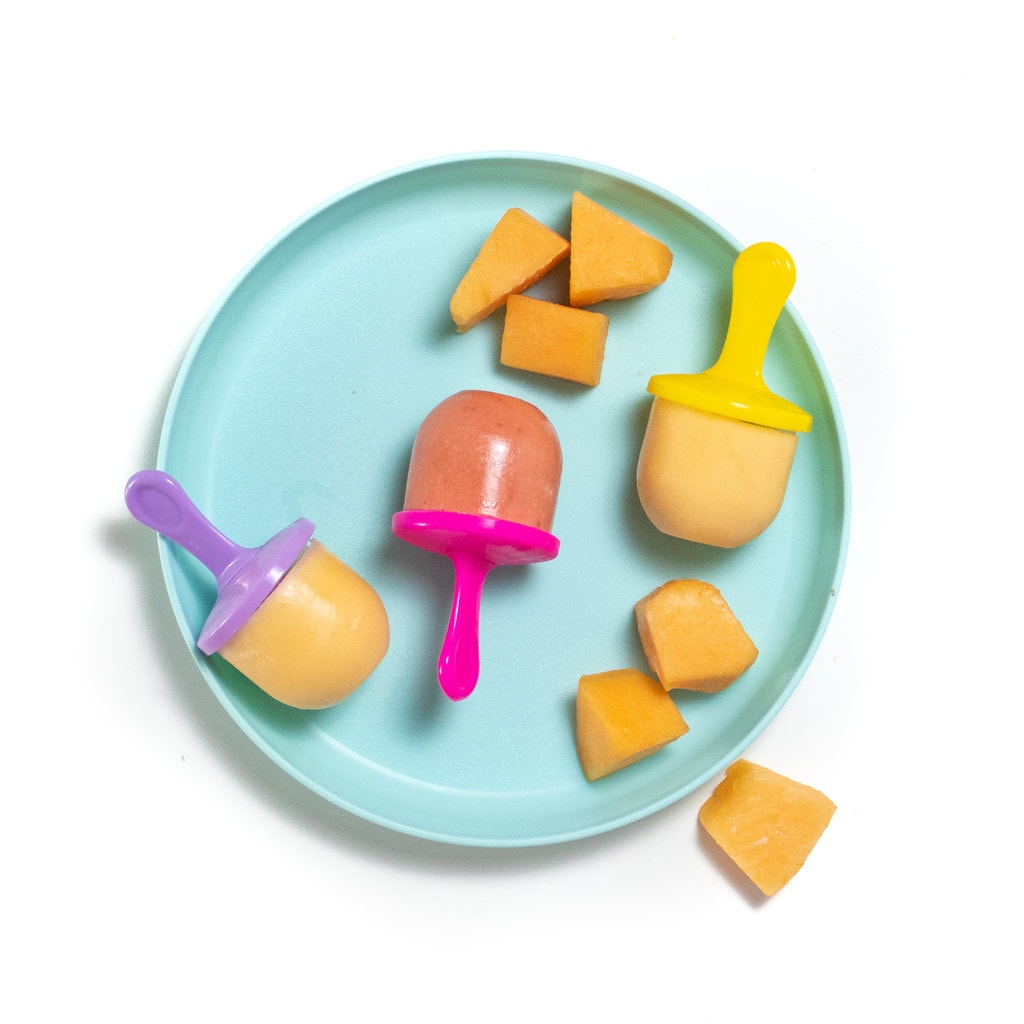 a teal kids play with colorful popsicle sticks and Cantelope Popsicles with the second option of strawberry cantaloupe Popsicles with chunks of cantaloupe on the plate and white background.