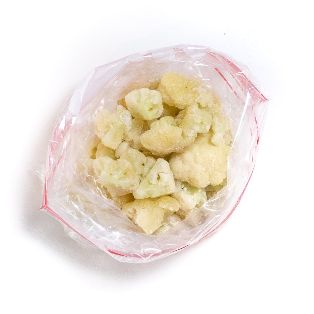 Plastic freezer bag filled with frozen cauliflower against a white backdrop.