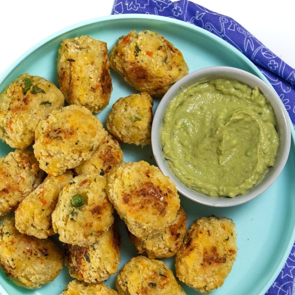 A teal kids plate full of cauliflower tots with a kids napkin against a white background.