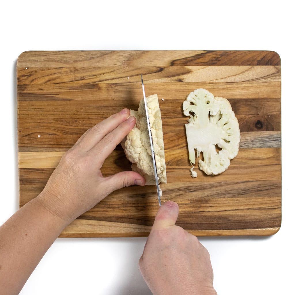 A pair of hands is cutting cauliflower steaks.