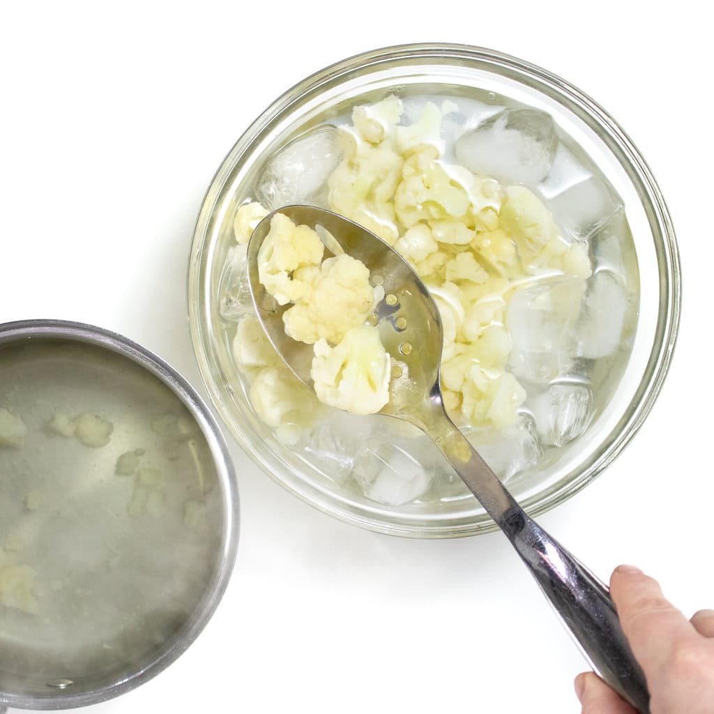 Bluish color flower being moved with a slotted spoon into an ice bath.