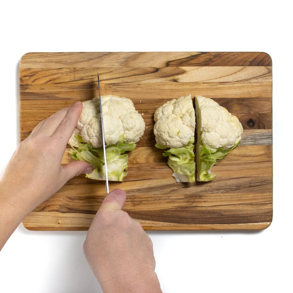 On a wooden cutting board two hands are cutting the color flower head into fourths.