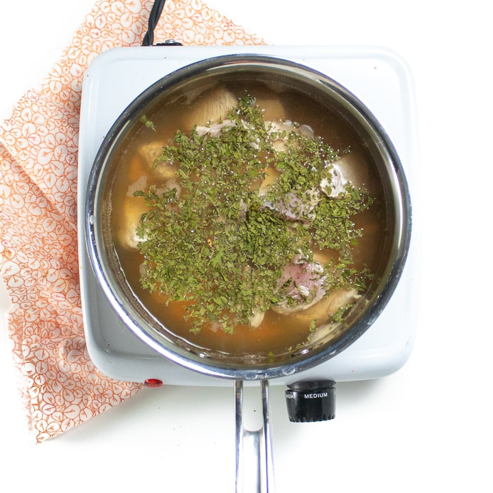 Saucepan full of broth, chicken and parsley. 